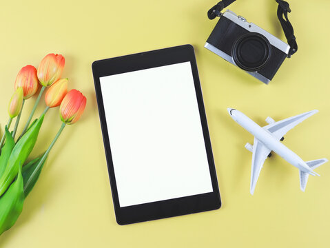 flat lay of digital tablet with blank white screen, tulip flowers, airplane model and  digital camera isolated on yellow background.