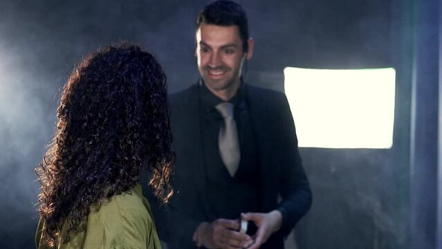 Magician talking to a female audience member on stage to perform a magic trick