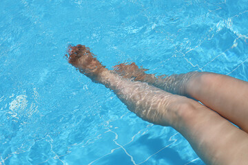 Female legs in the clear water of a swimming pool. Concept of foot care, vacation, wellness and spa