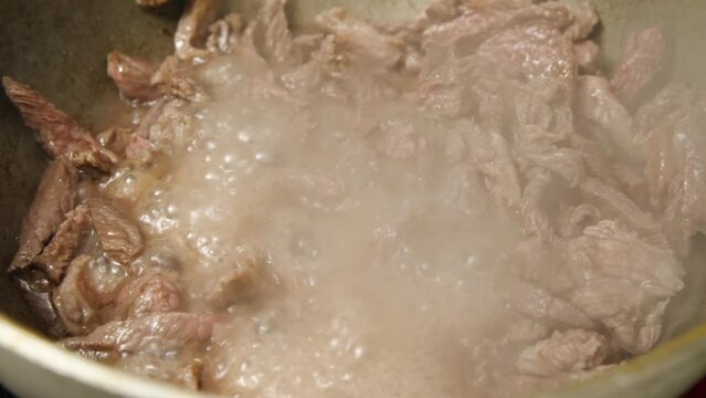 Close-up of slices of meat frying in the cauldron. The liquid is boiling and foaming, steam is rising. Cooking beef in a wok. Selective focus. Caucasian cuisine