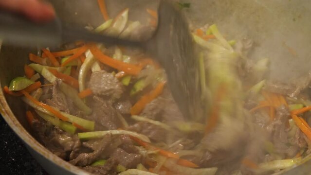 A close-up of the skimmer stirring the meat and vegetables that are roasting in the cauldron. Steam rises from the bottom. Caucasian or Asian cuisine. Selective focus