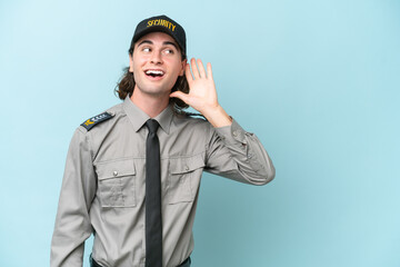 Young safeguard man isolated on blue background listening to something by putting hand on the ear