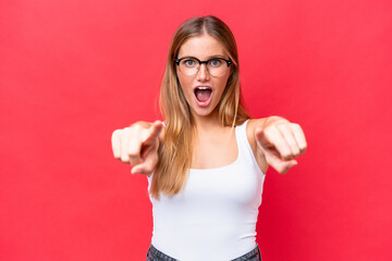 Young beautiful woman isolated on red background surprised and pointing front