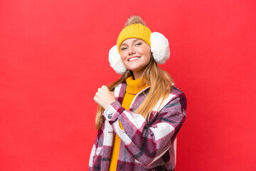 Young beautiful woman wearing winter muffs isolated on red background celebrating a victory