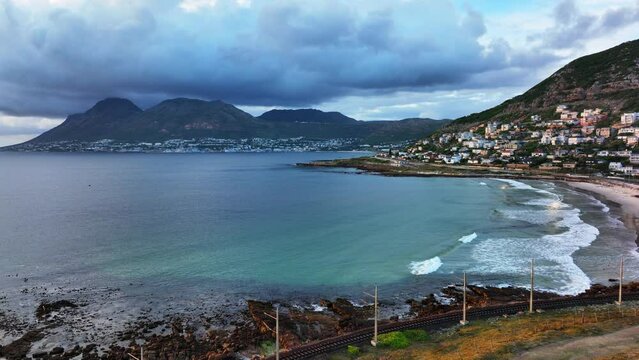 South African sunrise sunset morning Simon's Town drone aerial cinematic Fish Hoek rugged reef coast small fishing marina city stunning summer spring deep aqua blue ocean train tracks back movement