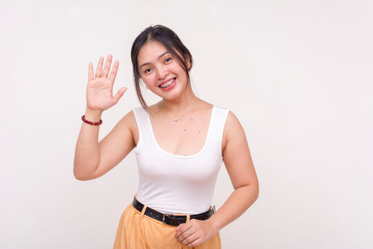 A friendly young Asian woman smiling and waving left hand to greet hello. Isolated on a white background.