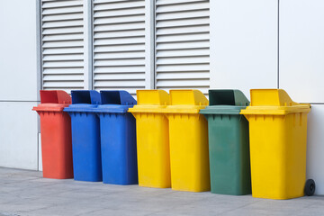 Yellow, green, blue and red recycling bins with separate recycling symbols on the building wall - 613773463