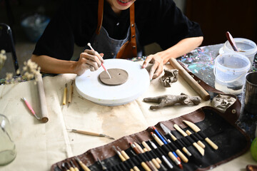 Young sculptor creating handmade ceramic plate on the pottery wheel in workshop. Indoors lifestyle activity, handicraft, hobbies concept