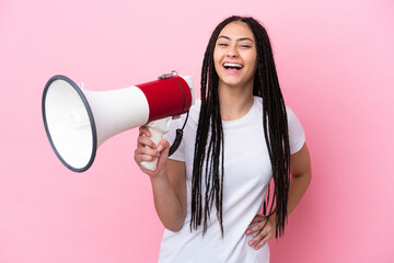 Teenager girl with braids over isolated pink background holding a megaphone and smiling