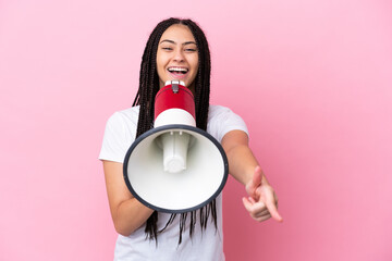 Teenager girl with braids over isolated pink background shouting through a megaphone to announce...