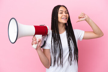Teenager girl with braids over isolated pink background holding a megaphone and proud and...