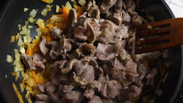Top view of a woman's hand in a wok with fried onions and carrots poured Chicken Gizzard and stirred with a wooden spatula. Close-up. Cooking in the Asian style
