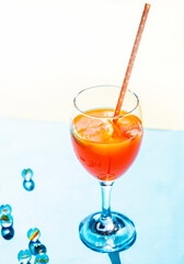 Glass with orange color cocktail with lemon and ice on blue white background with small glass balls isolated vertical 