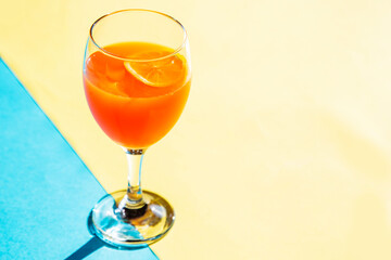 orange color cocktail with lemon on blue and yellow background with copy space 