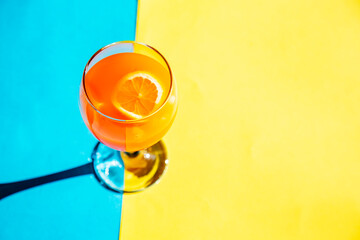 orange color cocktail with lemon on blue and yellow background with copy space 