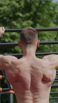Back view slow motion of shirtless muscular sportsman doing pull ups on horizontal ladder during fitness workout on sports ground Vertical video