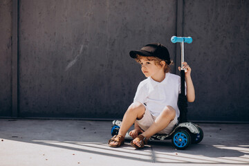 Cute little boy with curly hair riding scooter