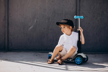 Cute little boy with curly hair riding scooter © Petro