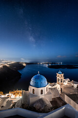 Night time image with stars and milky way of white and blue church with view on the caldera cliff and cruise ships on the Greek island of Santorini