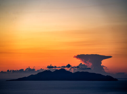 High altitude cloud with mushroom shape stretching at the top over the small greek island Anafi. Seen during sunrise, illuminating the cloud in red colours
