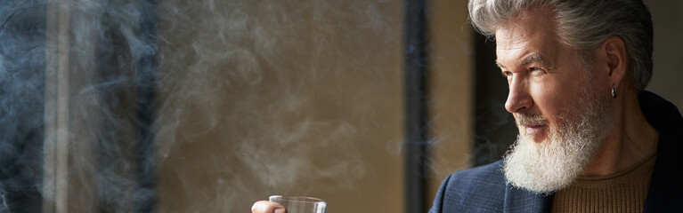 Portrait of sophisticated mature businessman with beard looking away while holding glass of whisky...
