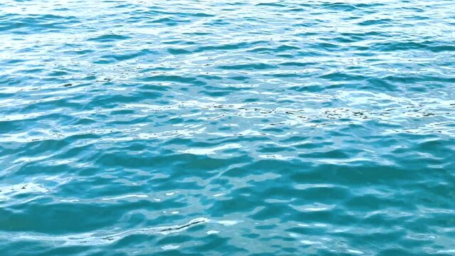 The sea, the water surface. Smooth swaying of the waves. The blue-green surface of the ocean. Light ripples on the surface of the water. Close-up. Natural background.