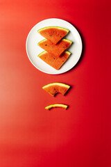 Melonen Stücke auf einem weißen Teller in einer Reihe. Roter Tisch, Flat lay, minimalistisch.