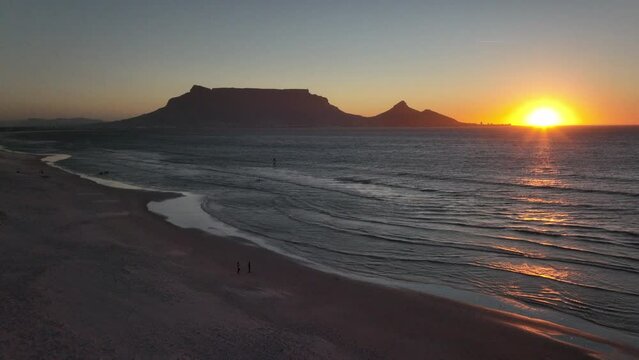 Cape Town South Africa family people walking on sand windy surf wave Table Mountain drone aerial cinematic Lions Head sunset beach stunning mountain and ocean landscape orange gold sun backward motion