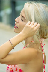PRETTY GIRL WITH BLONDE HAIR AND WEARING A PINK AND RED DRESS IS SMILING AND TOUCHING HER HAIR WITH HER HAND