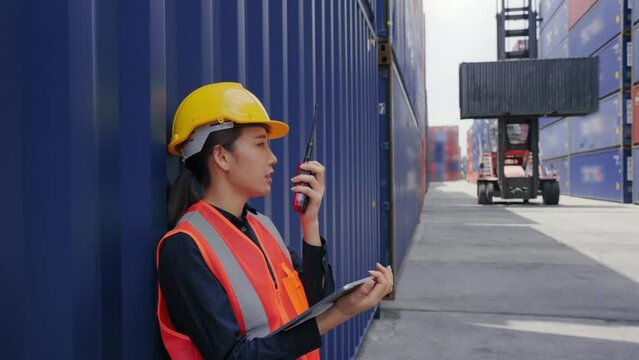 Asian manager worker female calling via walkie talkie while control driver forklift at transport warehouse. Cargo and Logistic shipping concept