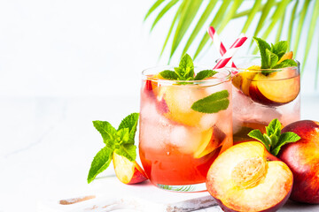 Peach cocktail, iced peach tea, fruit drink with fresh fruits and tropical leaves..