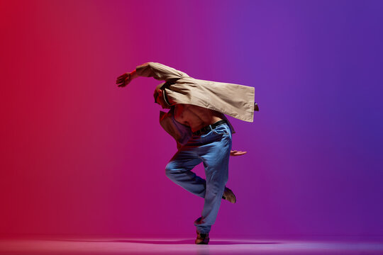 Young sportive man, in stylish casual clothes dancing breakdance, hip-hop against pink purple studio background. Muscular body. Concept of art, street style dance, fashion, youth, hobby, dynamics, ad