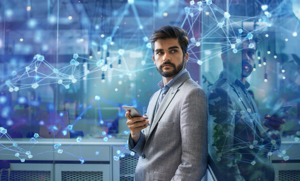 Portrait of handsome young businessman with smart phone standing in office with hologram background. Business, communication and technology concept. - Powered by Adobe
