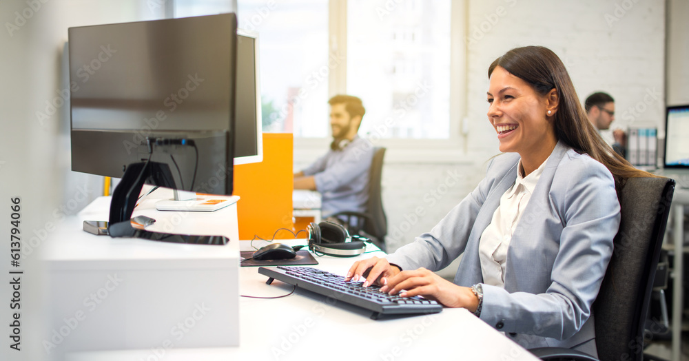 Wall mural Happy female employee in suit using computer at office.