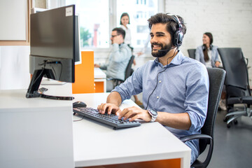 Handsome male customer support phone operator with headset working in call center.