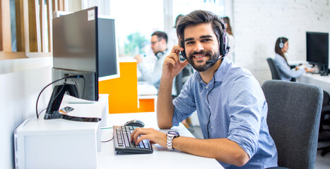 Portrait of handsome smiling young man working in a call center with his colleagues in the...