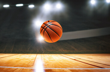 Basketball lying on wooden floor of basketball court and illuminated by spotlights