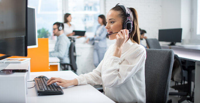 Brunette female customer service representative in a headset consulting clients online. Call center, business, people and technology concept
