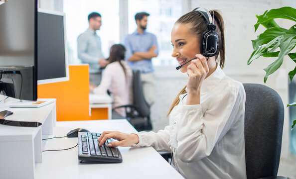 Beautiful Female Consultant Of Call Center In Headphones Working On Computer At Office.