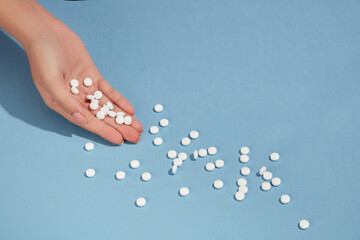 Woman's hand with white round pills on a blue background. Blank space for text addition. Suicide...