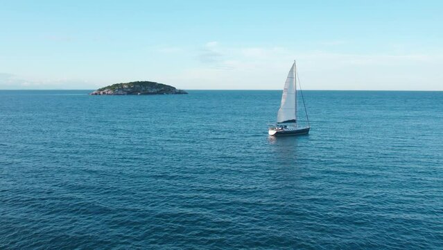 Small Sailboat Sails at Joao Fernandes Beach, Rio de Janeiro Brazil, Tropical Blue Water and Green Lonely Island in the Ocean, Aerial Drone Shot