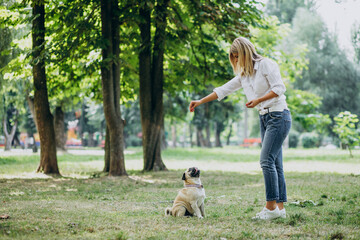 Naklejka na ściany i meble Woman having a walk in park with her pug-dog pet