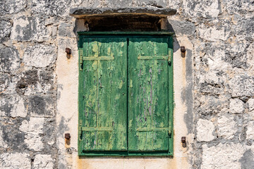 Typical old house with weathered closed green wooden shutters and stone wall, Rogoznica village, Dalmatia, Croatia