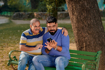 Young indian man showing some detail in smartphone to his father at park