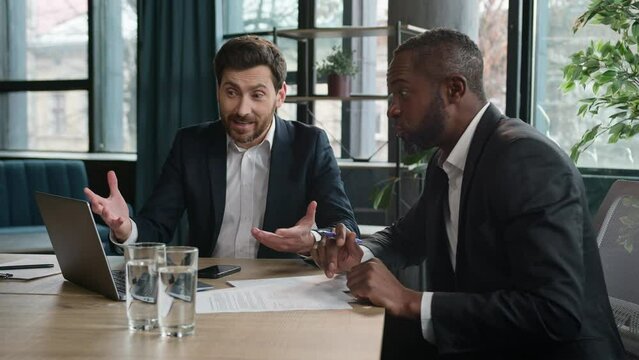 Happy excited two diverse businessmen multiethnic partners multiracial satisfied men enthusiastic partners at office meeting negotiate discuss good result business success with laptop computer data