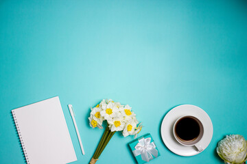 A blank notebook and cup of coffee with flowers over the green table.
