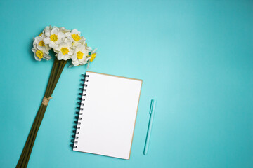 A white notebook and flowers over the mint background with copy space. 