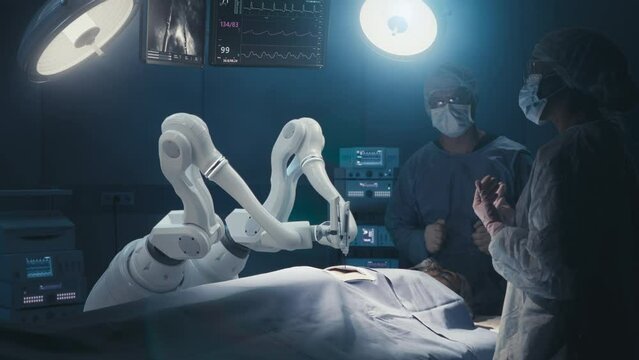 Two Surgeons Observing High-Precision Programmable Automated Robot Arms Operating Patient In Futuristic Hospital. Robotic Limbs Performing Advanced Nanosurgery, Doctors Looking At Vitals On Monitor