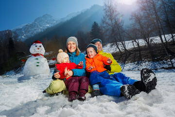 Family with two kids have fun in snow, over snowman and mountain