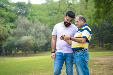 Young indian man showing some detail in smartphone to his father at park